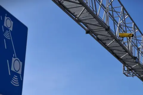 Niebieski znak informuje o odcinkowym pomiarze prędkości S7. Żółta kamera zamontowana na konstrukcji nad drogą rejestruje pojazdy.