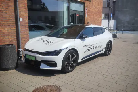 Biały samochód elektryczny Kia z napisem "#GOelectric D do 528 km zasięgu" informuje, ile prądu zużywa samochód elektryczny.
