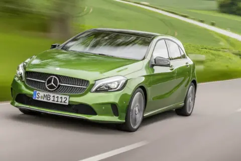 Zielony Mercedes klasy C pędzi po krętej drodze wśród zielonych pól.