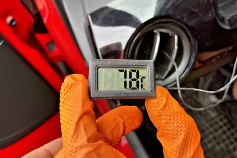 Rękawiczki w kolorze pomarańczowym trzymają termometr pokazujący 78°F. To część samodzielnego nabijania klimatyzacji.