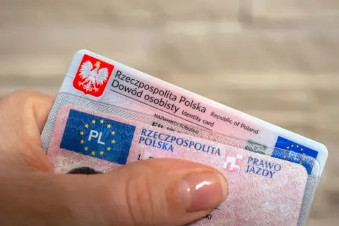 Dłoń trzyma polski dowód osobisty i prawo jazdy. Czy prawo jazdy bezterminowe trzeba wymienić? Sprawdź przepisy!