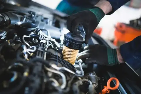 Mechanik w czarnych rękawiczkach wymienia filtr paliwa w silniku diesla.