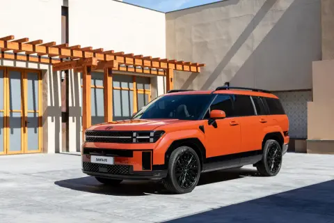 Pomarańczowy SUV Hyundai Santa Fe z czarnymi dodatkami i felgami, zaparkowany przed budynkiem z drewnianą pergolą.