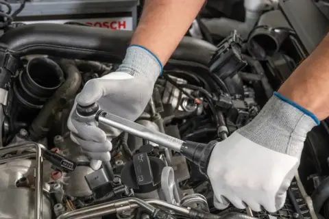 Mechanik w białych rękawiczkach dokonuje precyzyjnej wymiany świec w silniku samochodu, używając klucza dynamometrycznego.