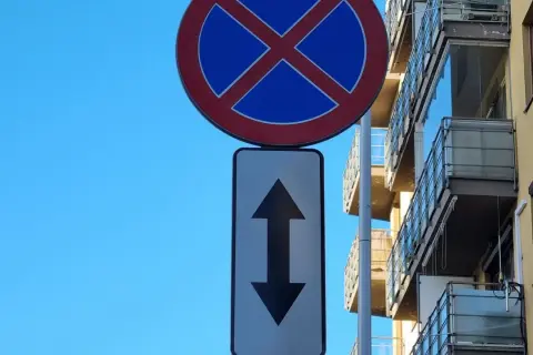 Znak zakazu zatrzymywania ze strzałką w górę i w dół, wskazującą na zakaz postoju w obu kierunkach.