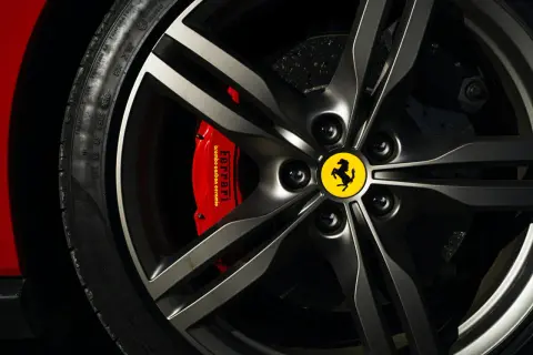 Logo samochodu ze skrzydłami na feldze Ferrari. Czerwony zacisk hamulcowy z napisem "Ferrari".