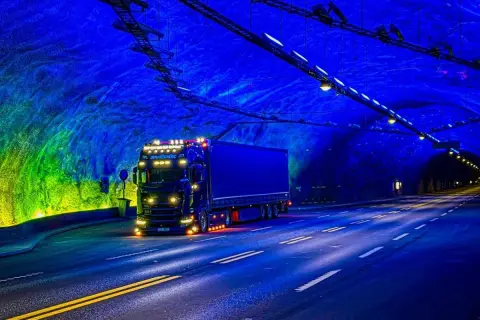 Ciężarówka jedzie przez najdłuższy tunel drogowy na świecie, oświetlony niebieskim i zielonym światłem.