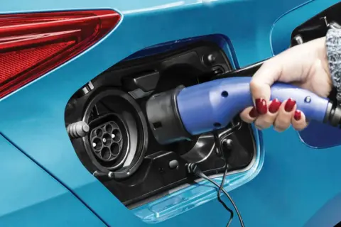 Dłoń z czerwonym lakierem na paznokciach podłącza ładowarkę do samochodu plug-in hybryda.