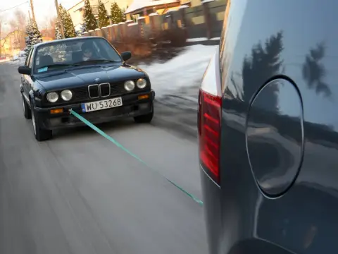 Czarny BMW holowany przez inny samochód, bo zabrakło paliwa. Co zamiast plaka do odpalenia? Lina holownicza!