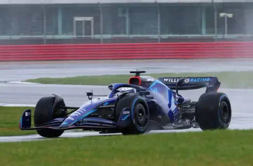 Niebieski bolid Formuły 1 z logo Williams Racing na torze w deszczu. Kierowcy formuły 1 muszą być odważni w takich warunkach.
