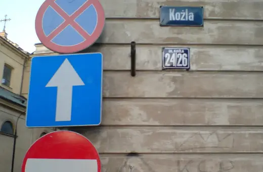Znaki drogowe z opisem: zakaz zatrzymywania, nakaz jazdy prosto, tabliczka z nazwą ulicy "Kozła" i numerem 24/26.