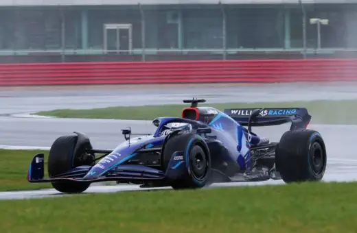 Niebieski bolid Formuły 1 z logo Williams Racing na torze w deszczu. Kierowcy formuły 1 muszą być odważni w takich warunkach.