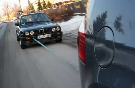 Czarny BMW holowany przez inny samochód, bo zabrakło paliwa. Co zamiast plaka do odpalenia? Lina holownicza!