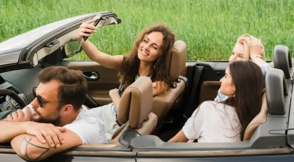 Radosne zwiedzanie Roztocza samochodem. Uśmiechnięta dziewczyna robi selfie z przyjaciółmi w kabriolecie, otoczeni zielenią.