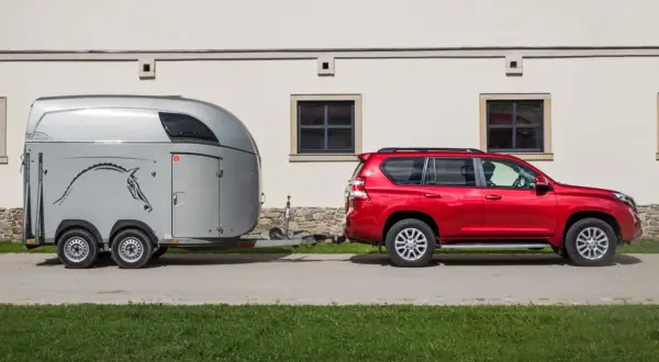 Czerwony SUV holuje przyczepę z koniem. B+E co daje? Możliwość przewiezienia ukochanego zwierzęcia w komfortowych warunkach.