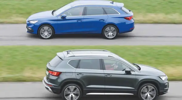 Dwa samochody klasy D: niebieskie kombi i ciemnoszary SUV, jadące obok siebie po drodze.