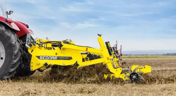 Czerwony traktor z żółtym agregatem uprawowym Bednar Terraland pracuje na polu.