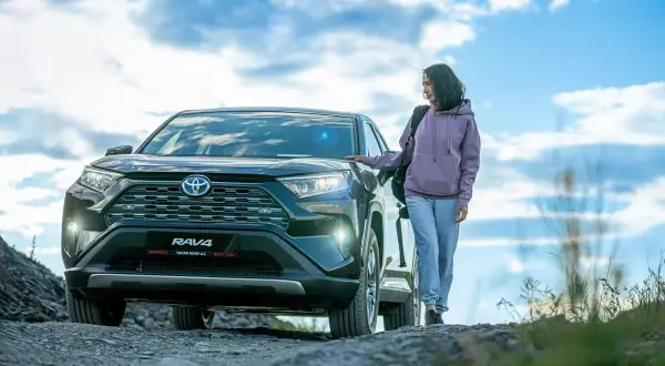 Kobieta obok Toyoty RAV4, jednego z najmniej awaryjnych crossoverów, na tle nieba z chmurami.