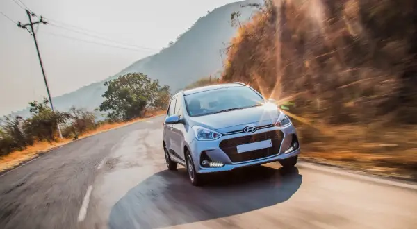 Srebrny Hyundai przemierza krętą drogę w słoneczny dzień. Ten Hyundai z jakiego kraju pochodzi? Z Korei Południowej, gdzie powstała ta marka.