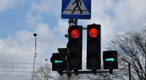 Sygnalizacja świetlna: czerwone światła dla jazdy prosto, zielona strzałka w lewo. Czy na strzałce w lewo można zawracać? Znak przejścia dla pieszych.