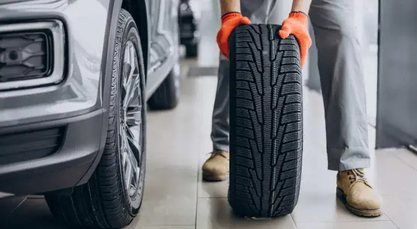 Mechanik w pomarańczowych rękawiczkach trzyma nowe opony letnie obok samochodu. Czas na test opon letnich!