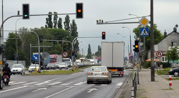 Kierowca srebrnego sedana decyduje się na przejazd na żółtym świetle, mimo że sygnalizator obok świeci na czerwono.