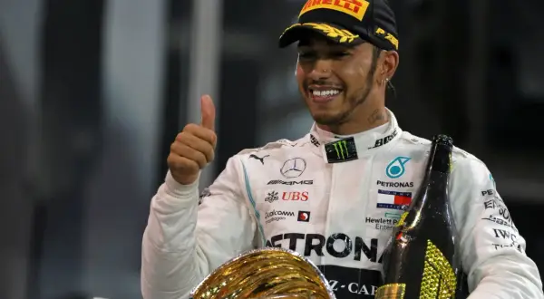 Lewis Hamilton, jeden z najlepsi kierowcy f1, świętuje zwycięstwo z pucharem i szampanem, pokazując kciuk w górę.