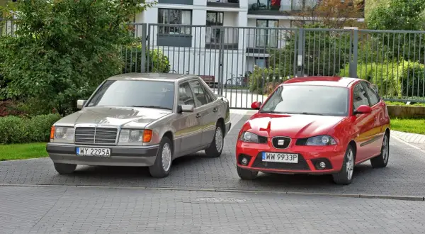 Dwa samochody, srebrny Mercedes i czerwony Seat, stoją obok siebie. To tylko mała część rosnącej ilości samochodów w Polsce.