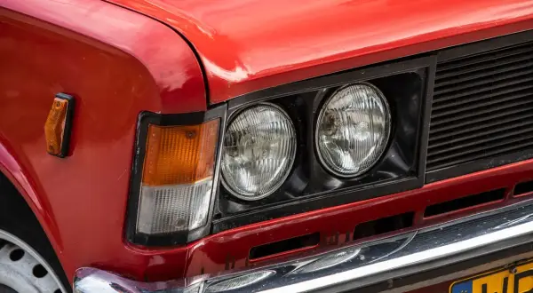 Czerwone auto z włoch, z podwójnymi okrągłymi reflektorami i pomarańczowym kierunkowskazem.
