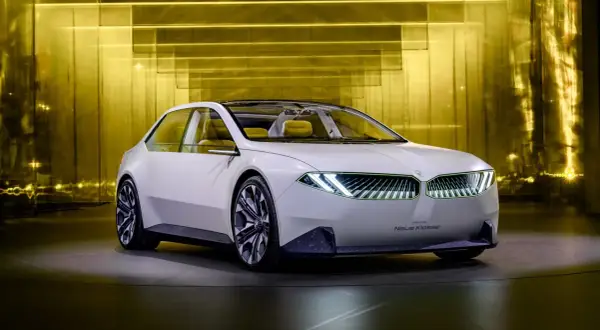 Biały koncept BMW Neue Klasse z futurystycznymi światłami i żółtym wnętrzem, prezentowany na tle złotej, lśniącej ściany.