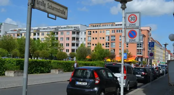 Ulica w Niemczech z kolorowymi kamienicami, znakami drogowymi (w tym fotoradary w niemczech) i zaparkowanymi samochodami.