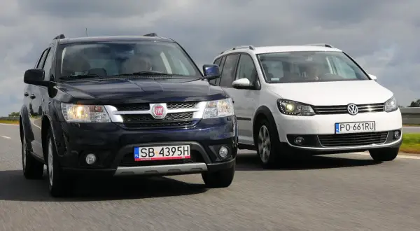 Dwa duże samochody rodzinne, ciemny Fiat i biały Volkswagen, jadą obok siebie po drodze.