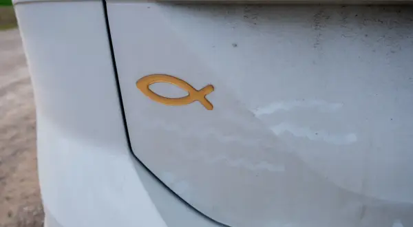 Złoty symbol ryby na białym samochodzie. To chrześcijański znak, który oznacza "Jezus Chrystus, Syn Boży, Zbawiciel".