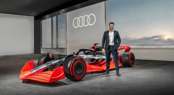 Mężczyzna w garniturze obok futurystycznego bolidu Audi F1 2026.
