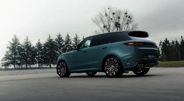 Elegancki, zielony Range Rover, jeden z prestiżowych angielskich marek samochodów, parkuje na tle drzew.