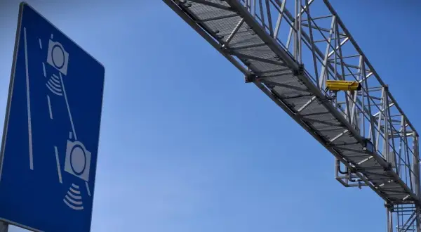 Niebieski znak informuje o odcinkowym pomiarze prędkości S7. Żółta kamera zamontowana na konstrukcji nad drogą rejestruje pojazdy.