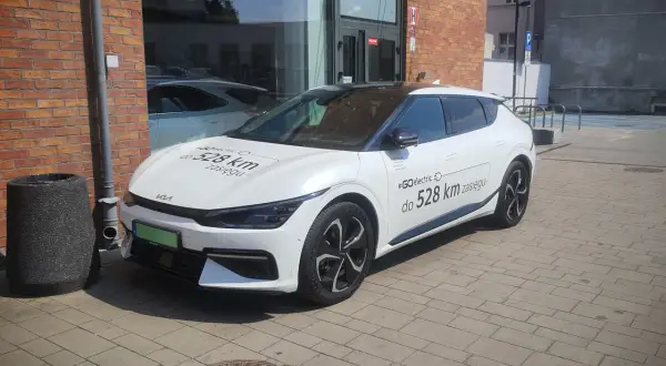 Biały samochód elektryczny Kia z napisem "#GOelectric D do 528 km zasięgu" informuje, ile prądu zużywa samochód elektryczny.