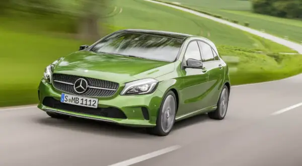 Zielony Mercedes klasy C pędzi po krętej drodze wśród zielonych pól.