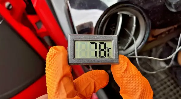 Rękawiczki w kolorze pomarańczowym trzymają termometr pokazujący 78°F. To część samodzielnego nabijania klimatyzacji.