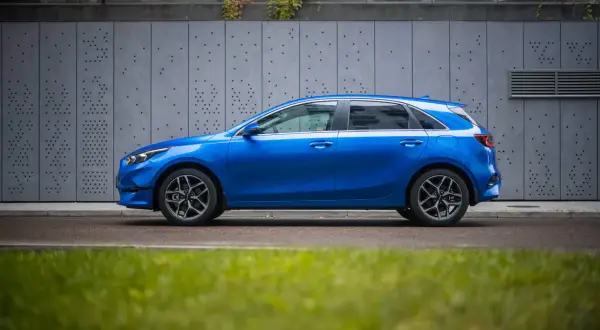 Niebieski hatchback z dynamiczną linią nadwozia, przypominającą coupe, zaparkowany przy nowoczesnej, szarej ścianie.