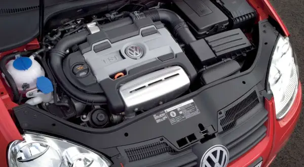 Silnik 1.4 TSI Twincharger w czerwonym Volkswagenie. Widoczny jest blok silnika z logo VW, przewody i elementy układu dolotowego.