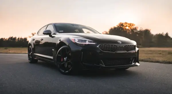 Czarna Kia Stinger, sportowy samochód z Korei Południowej, zaparkowana na pustej drodze o zachodzie słońca.
