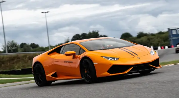 Pomarańczowe Lamborghini z czarnymi pasami na masce podczas szybkiego przejazdu po torze wyścigowym.