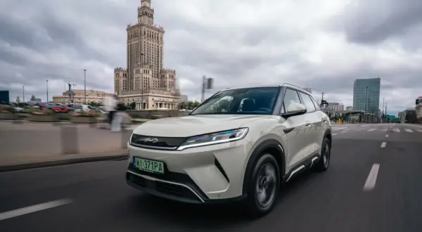 Biały SUV marki BYD, jeden z chińskich marek aut, jedzie ulicą Warszawy. W tle Pałac Kultury i Nauki.