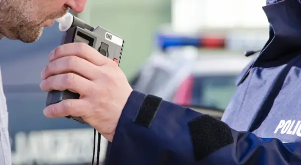 Mężczyzna dmucha w alkomat, który pokazuje wynik, mimo że nie pił. Policjant w mundurze z napisem POLICJA trzyma urządzenie.
