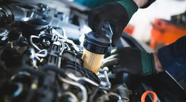 Mechanik w czarnych rękawiczkach wymienia filtr paliwa w silniku diesla.