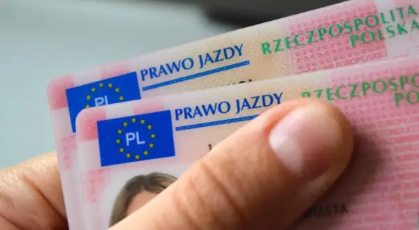 Dłoń trzyma dwa nowe polskie prawo jazdy. Widoczne napisy "PRAWO JAZDY" i godło UE.