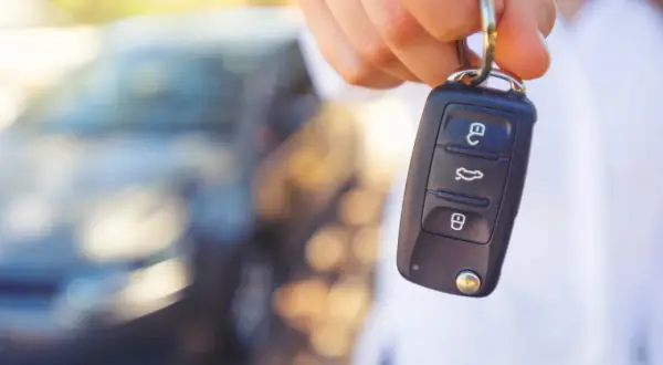 Kluczyk samochodowy z przyciskami, sugerujący jak wyłączyć immobilizer. W tle rozmyty samochód.