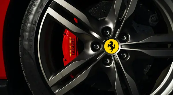 Logo samochodu ze skrzydłami na feldze Ferrari. Czerwony zacisk hamulcowy z napisem "Ferrari".