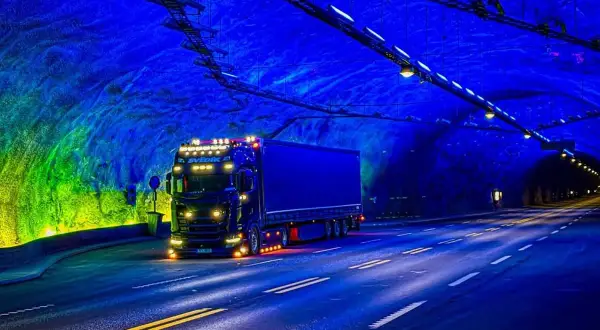 Ciężarówka jedzie przez najdłuższy tunel drogowy na świecie, oświetlony niebieskim i zielonym światłem.